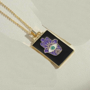 Detail der Makroansicht von goldenem Hamsa-Hand und lila Evil Eye Emaille-Anhänger