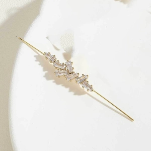 Macro shot of gold ear hook with rectangular step-cut zircon crystals on white ceramic