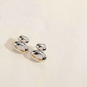 Detailed view of polished silver double pebble earrings on a beige textured background