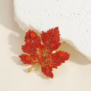 Macro detail van esdoornblad broche met rode strass steentjes en goudkleurige afwerking