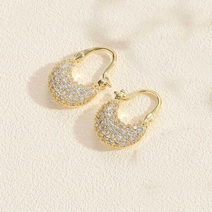 Gros plan sur des boucles d'oreilles en C dorées avec micro-pavage de zircons blancs