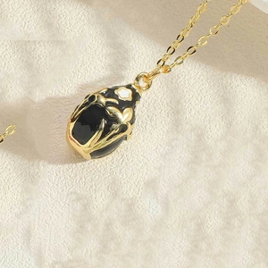 Macro shot of an oval black enamel pendant with golden floral motifs on a fine chain