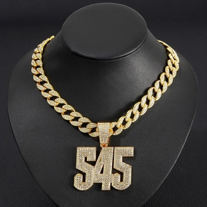 Gros plan du pendentif doré chiffre 545 serti de strass sur une chaîne maille cubaine