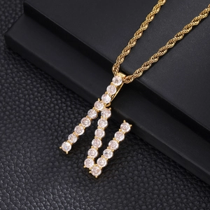 Macro detail of gold-plated letter M pendant with iced-out cubic zirconia on rope chain