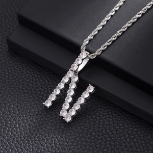 Macro shot of silver-colored iced out letter M pendant with zircon stones and rope chain