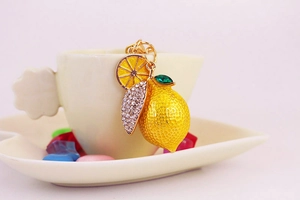 Detailed view of yellow lemon keychain with sparkling rhinestone leaf on white coffee cup
