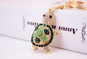 Detail of cute turtle keychain with sparkling green and white rhinestones on golden alloy