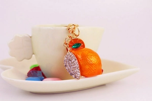 Detail of a gold orange fruit keychain with orange enamel and sparkling crystals