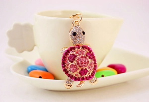 Close-up of pink crystal sea turtle keychain leaning on a white coffee cup