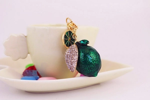 Detail of green lime keychain with rhinestones and gold clasp hanging on white coffee cup
