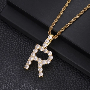 Macro view of iced out letter R pendant with cubic zirconia stones on gold rope chain