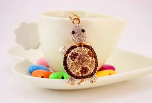 Close-up of a rhinestone-studded turtle keychain hanging on a white porcelain cup edge