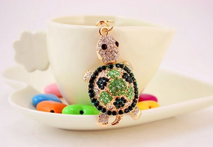 Macro detail of a green rhinestone turtle keychain leaning against a white coffee cup