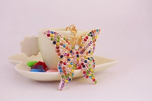 Détail d'un porte-clés papillon en strass colorés posé sur une soucoupe blanche en cœur
