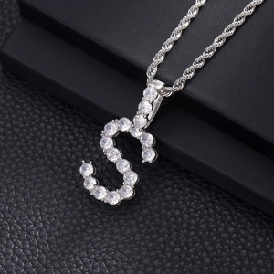 Macro shot of silver-colored capital S pendant with clear zircon pave and rope chain