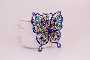 Vue détaillée porte-clés papillon doré avec strass bleus et verts sur tasse blanche