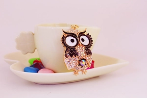 Detail einer Eulen-Schlüsselanhänger mit weißen und lila Strasssteinen an einer Tasse