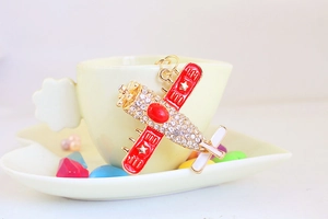 Detail of red enamel airplane keychain with sparkling rhinestones on a coffee cup