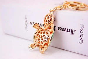 Detail of golden turtle keychain with heart cut-outs and green enamel on book
