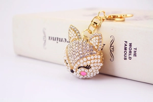 Détail macro d'un porte-clés renard doré avec perles blanches, strass et clin d'œil