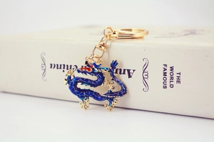 Detail of a golden dragon keychain with blue enamel inlay resting on a white book