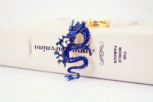 Detailed blue enamel Chinese dragon keychain with gold ring resting on a white book