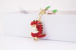 Detail shot of a red rhinestone dinosaur keychain hanging on a white gift box