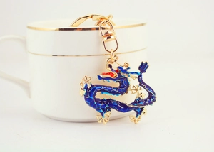 Detailed close-up of golden metal dragon keychain with dark blue enamel finish