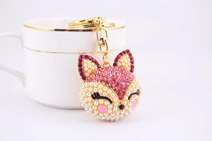Détail du porte-clés renard doré orné de cristaux roses et perles sur une tasse de café