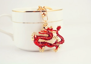 Close-up of a red enamel Chinese dragon keychain hanging on a white coffee cup