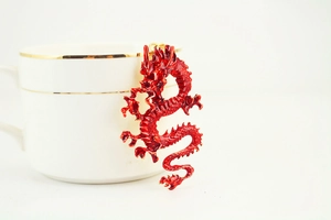 Detail of red enamel Chinese dragon charm hanging on a white ceramic cup edge