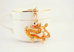 Detailed close-up of a golden dragon keychain with yellow enamel on a white coffee cup