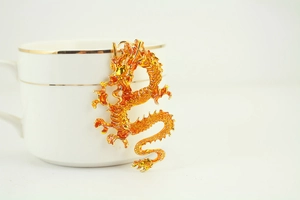 Detailed close-up of a dragon keychain with yellow enamel finish on a white ceramic cup