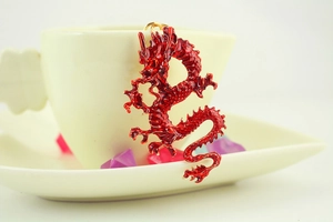 Detailed macro of a red enamel Chinese dragon pendant hanging on a white coffee cup