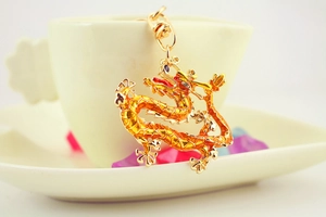 Detail of a golden dragon keychain with red enamel scales hanging on a white ceramic cup