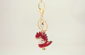 Close-up of a red rhinestone dinosaur keychain with polished gold lobster clasp hardware