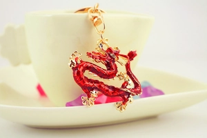 Close-up of golden Chinese dragon keychain with red enamel details hanging on a ceramic cup