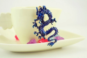 Close-up of a blue enamel dragon keychain with gold-plated edges hanging on a ceramic cup