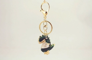 Close-up of a sparkling gold-plated dinosaur keychain with green rhinestones and enamel belly