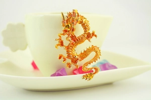 Detailed view of a golden Chinese dragon pendant with scale texture on a ceramic cup