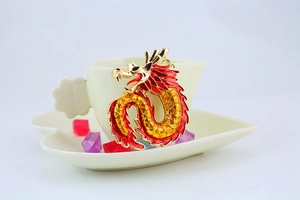Detalle de llavero de dragón dorado con esmalte rojo en el borde de una taza