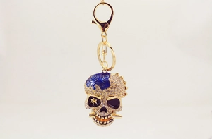 Détail d'un porte-clés tête de mort doré avec strass blancs et couronne en émail bleu