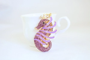 Macro detail of seahorse charm with purple crystals and gold alloy finish on white cup