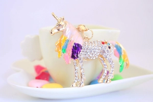 Close-up of a sparkling rhinestone unicorn keychain with rainbow enamel on a ceramic cup