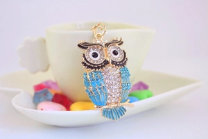 Détail du porte-clés hibou avec strass bleus accroché à une tasse à café crème