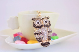 Détail d'un porte-clés hibou doré avec strass brillants posé contre une tasse à café