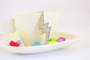 Detail of lightning-shaped gold keychain with sparkling blue and purple crystals on a cup