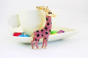 Close-up of a pink rhinestone giraffe keychain leaning against a white coffee cup
