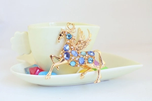 Detailansicht eines goldenen Pegasus-Anhängers mit blauen Strasssteinen auf Keramik