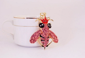 Detalle de llavero de abeja con pedrería rosa y corona roja en una base dorada